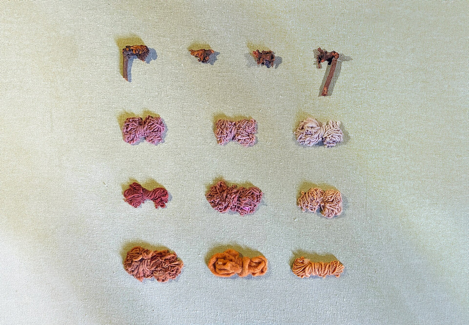 Assorted small yarn balls on a textured beige surface showing color of Rubia tinctorum (madder) natural dye