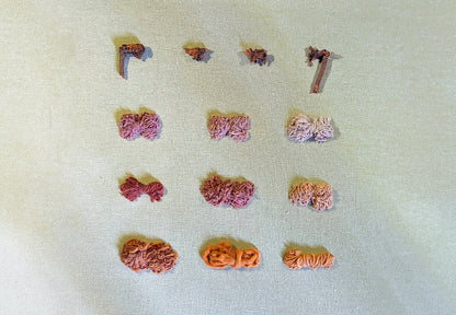Assorted small yarn balls on a textured beige surface showing color of Rubia tinctorum (madder) natural dye